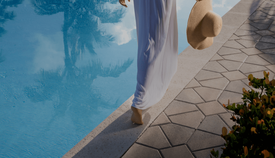 Person walking along the edge of a crystal clear pool with a hat in hand