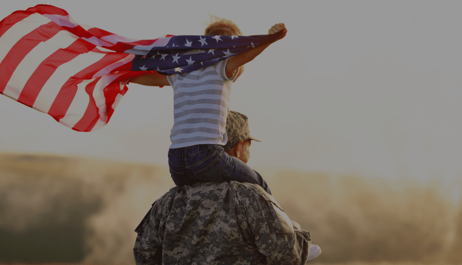 Child holding an American flag sitting on top of a military member's shoulders