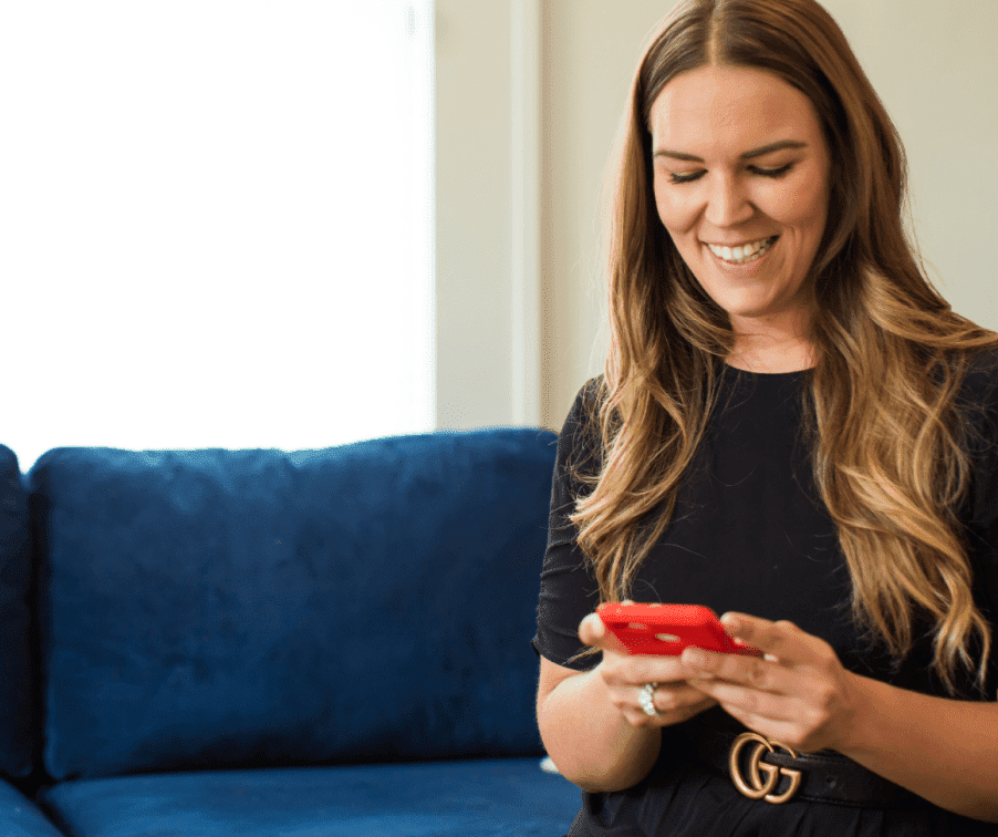 Photo of a woman sitting on a couch, smiling, reading something off her iPhone.